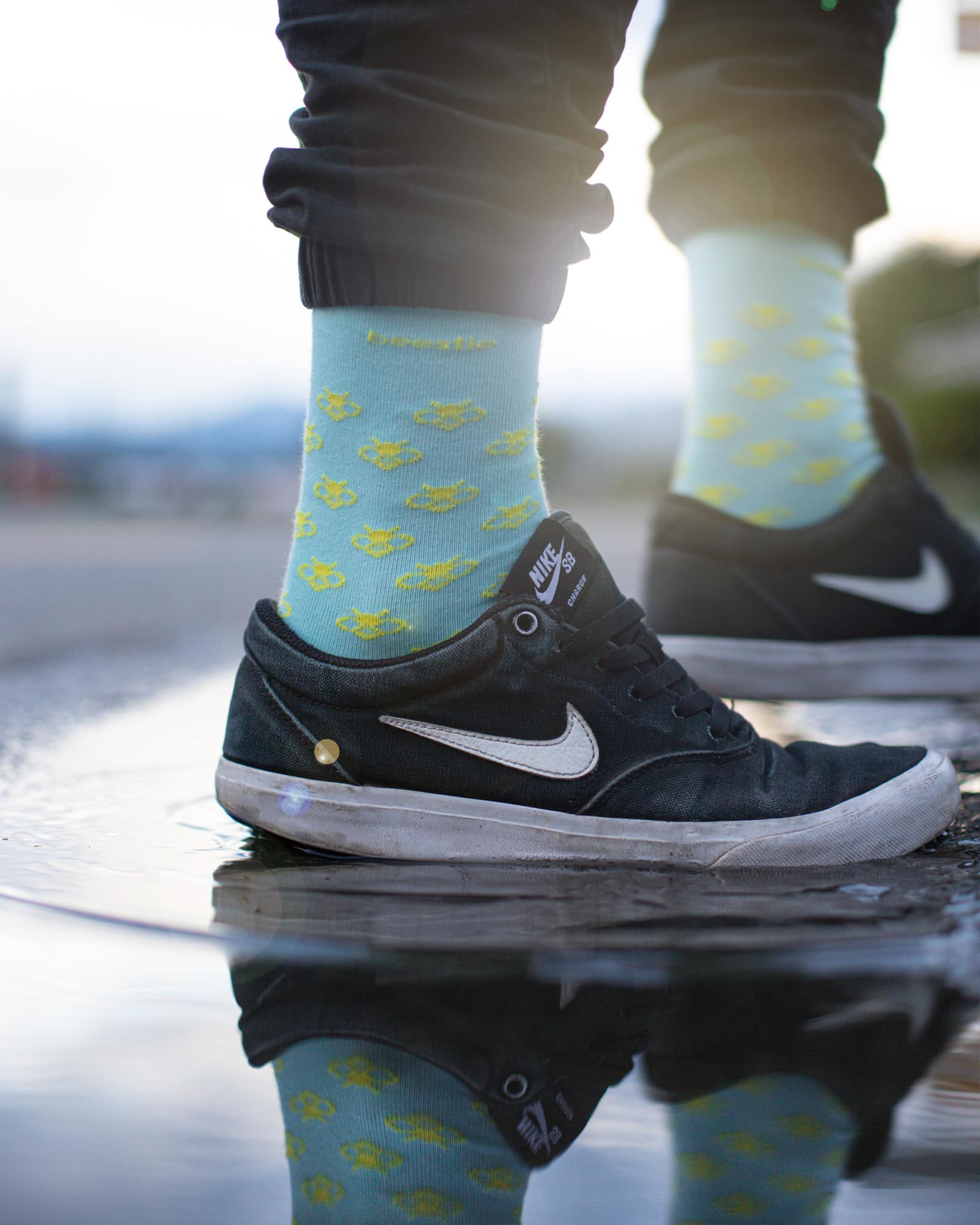 beestie Socken hellblau mit gelben Bienen steht in Pfütze mit Nike Schuhen